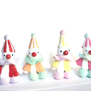 May include: Four small, handmade clown figurines. Each clown has a white face, red nose, and a colorful outfit. The hats and outfits are striped in red, orange, yellow, and pink. The clowns have a whimsical, playful design.