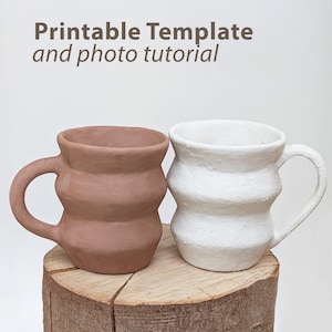 May include: Two handmade ceramic mugs, one in a terracotta color and the other in white, sit side-by-side on a wooden surface. The mugs have a unique, wavy design and attached handles. The text "Printable Template and photo tutorial" is at the top.