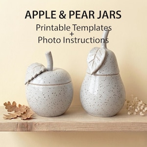 May include: Two speckled ceramic jars, one apple-shaped and one pear-shaped, sit on a wooden shelf. The apple jar has a stem and leaf handle, while the pear jar has a leaf-shaped handle. The text "APPLE & PEAR JARS" is at the top.