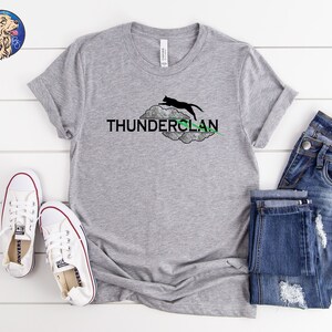 May include: A gray t-shirt with a black cat jumping over a cloud with the text "THUNDERCLAN" in black letters. The cloud has a green lightning bolt.