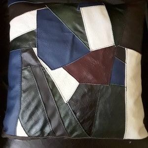 May include: A patchwork pillow cover made from different colored leather pieces. The cover features shades of white, brown, dark green, blue, and black leather.