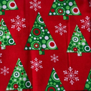 May include: Red fabric with a repeating pattern of green Christmas trees with white circles and red dots. White snowflakes are scattered throughout the fabric.