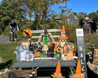 May include: A table display of handmade Halloween decorations for sale. The decorations include witches, pumpkins, cats, and crows. The sign reads "For Sale".