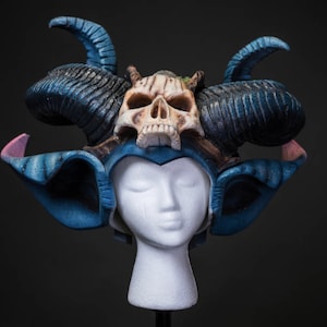 May include: A blue and white costume headpiece with horns and a skull. The skull is painted in a bone color with black eyes and a black mouth.