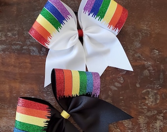 May include: Two hair bows with a rainbow glitter design. One bow is white and the other is black.