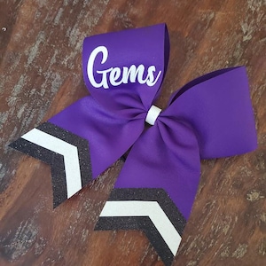May include: Purple cheer bow with black and white chevron stripes and the word "Gems" in white lettering.
