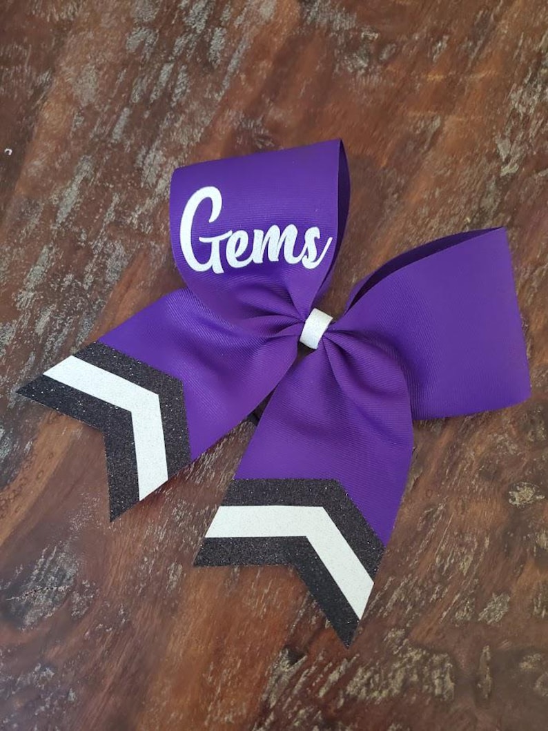 May include: Purple cheer bow with black and white chevron stripes and the word "Gems" in white lettering.