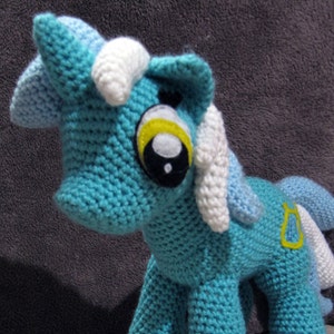 May include: A crocheted blue unicorn toy with white and yellow accents. The unicorn has a yellow horseshoe on its flank.