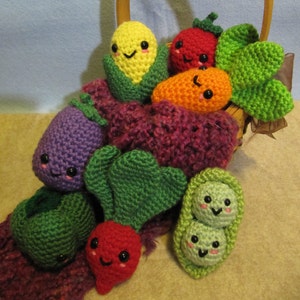May include: A crocheted basket filled with colourful crocheted vegetables, including a corn, tomato, carrot, aubergine, radish, and peas. The vegetables have cute faces and are arranged in a basket with a wooden handle.