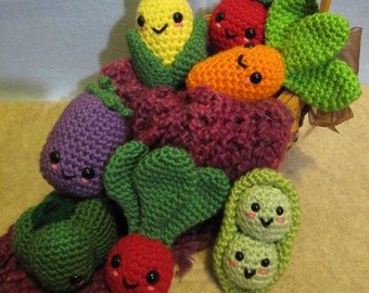 May include: A crocheted basket filled with colourful crocheted vegetables, including a corn, tomato, carrot, aubergine, radish, and peas. The vegetables have cute faces and are arranged in a basket with a wooden handle.