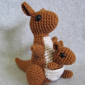 May include: A brown crocheted kangaroo holding a smaller brown crocheted joey in its pouch. Both kangaroos have black eyes.