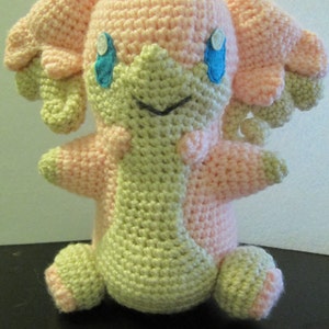 May include: A crocheted plush toy in pink and beige with blue eyes. The toy has a rounded body and long, floppy ears.