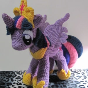 May include: Purple crocheted plush toy of Twilight Sparkle from My Little Pony. The toy has a yellow crown, pink and blue hair, and a purple, pink, and blue tail.