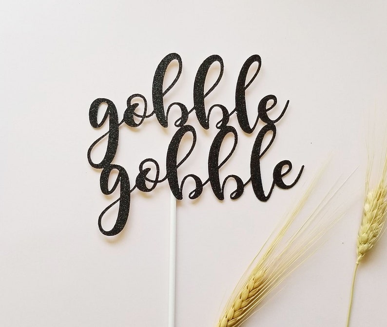 May include: Black glitter cake topper with the words "gobble gobble" in a cursive font.