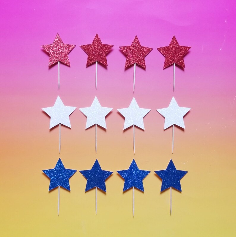 May include: Ten red, white, and blue star-shaped cake toppers. The stars are made of glitter paper and have a toothpick attached to the back.