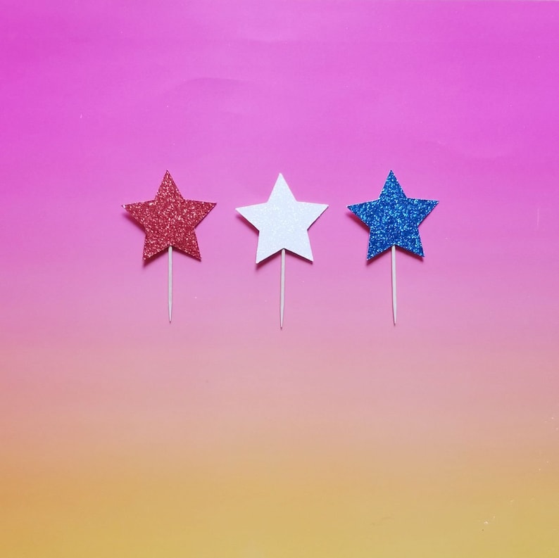 May include: Three glitter star-shaped cake toppers. The stars are red, white, and blue. The stars are on sticks.