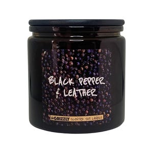Pode incluir: Vela em frasco de vidro preto com tampa preta. A vela tem um rótulo com uma descrição de aroma de pimenta preta e couro. O rótulo também diz "Grizzly Scented Soy Candle".