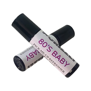 May include: Two black roll-on bottles with white labels. The label on the top bottle reads "80's Baby Pick-Me-Up Refresher". The label on the bottom bottle reads "80's Baby".