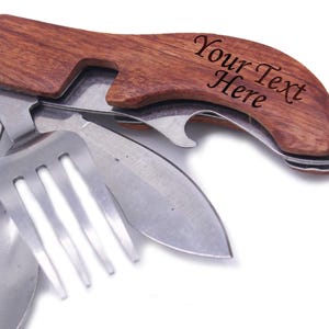 Puede incluir: Una herramienta multiusos con mango de madera, que incluye una cuchara, un tenedor, un cuchillo, un abridor de botellas y un mango de madera con el texto "Your Text Here" grabado en él.