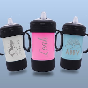 May include: Three personalised stainless steel sippy cups with different designs. The first cup is white with a mermaid design and the name "Olivia" engraved on it. The second cup is pink with the name "Leah" engraved on it. The third cup is blue with a rainbow and clouds design and the name "Abby" engraved on it.