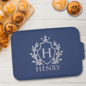 May include: A blue silicone baking mat with a silver design of a shield with the letter H and a crown above it. The text "HENRY." is below the shield.