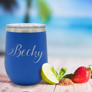 May include: A blue insulated tumbler with the name "Becky" in a cursive font. The tumbler is next to a lime wedge, mint leaves, a strawberry, and brown sugar. The background is a blurred beach scene.
