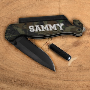May include: A camouflage patterned pocket knife with a black blade and a flashlight. The knife has a safety latch and a belt clip. The knife is personalized with the name "SAMMY" in white letters.