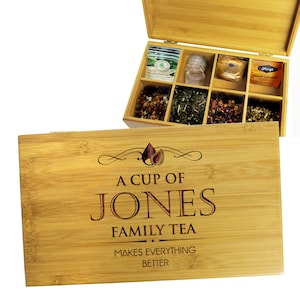 May include: A bamboo tea box with a hinged lid, containing various tea bags and loose leaf teas. The box is engraved with the text "A CUP OF JONES FAMILY TEA MAKES EVERYTHING BETTER". The box is made of light brown bamboo.
