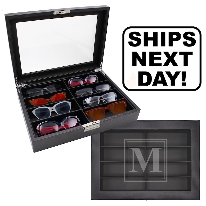 May include: A black rectangular eyewear storage case with a clear glass lid and eight interior compartments. The case features a textured exterior finish and a silver-toned metal latch. One view shows the case open with various sunglasses inside.