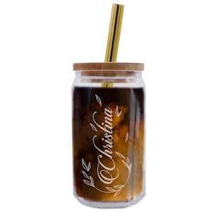 Puede incluir: Un vaso de vidrio transparente con una tapa marr&oacute;n y una pajita de metal dorado. El vaso contiene un l&iacute;quido marr&oacute;n y el nombre "Christina" est&aacute; grabado en el lateral en blanco.