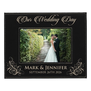 May include: Black photo frame with the text "Our Wedding Day" in elegant script. The frame features a photo of a couple on their wedding day. The names "Mark & Jennifer" and the date "September 26th 2026" are displayed at the bottom.
