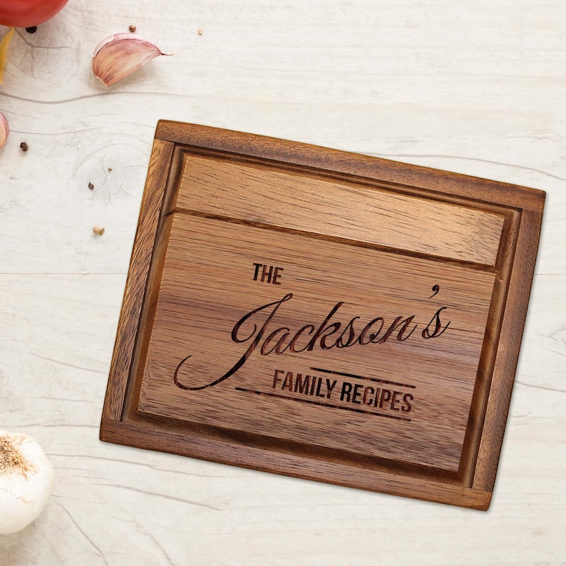 Pu&ograve; includere: Un tagliere rettangolare in legno con finitura marrone scuro e bordo scanalato. Il centro &egrave; inciso con il testo "THE Jackson's FAMILY RECIPES" in una combinazione di scrittura elegante e lettere sans-serif in grassetto maiuscolo.
