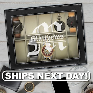 May include: A rectangular black watch display case with a glass lid featuring a white monogram letter M and the name Matthews printed on the center. The interior contains beige compartments holding five various wristwatches and a pocket watch.