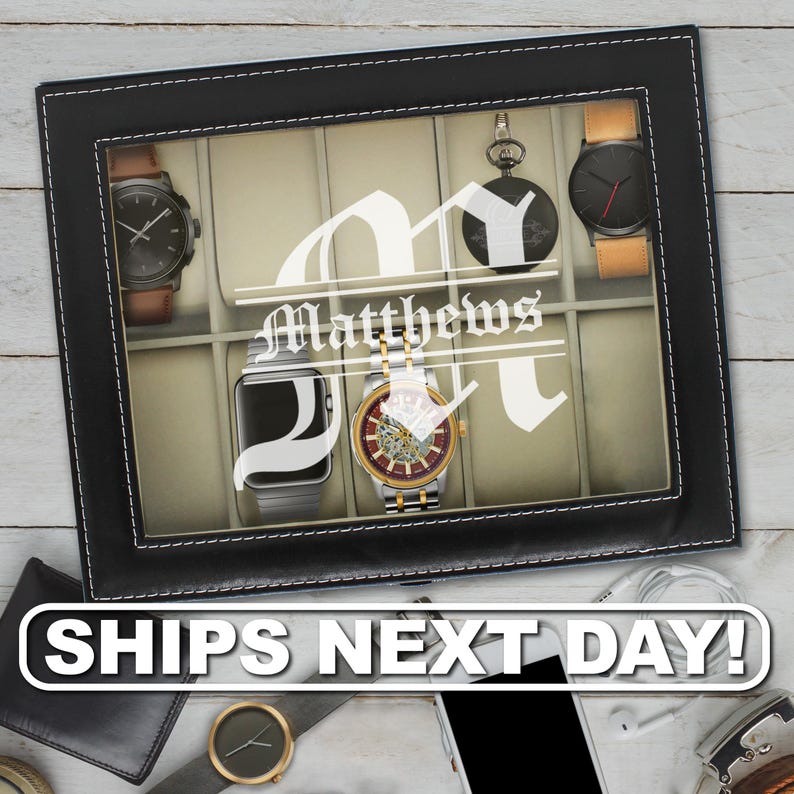 May include: A rectangular black watch display case with a glass lid featuring a white monogram letter M and the name Matthews printed on the center. The interior contains beige compartments holding five various wristwatches and a pocket watch.