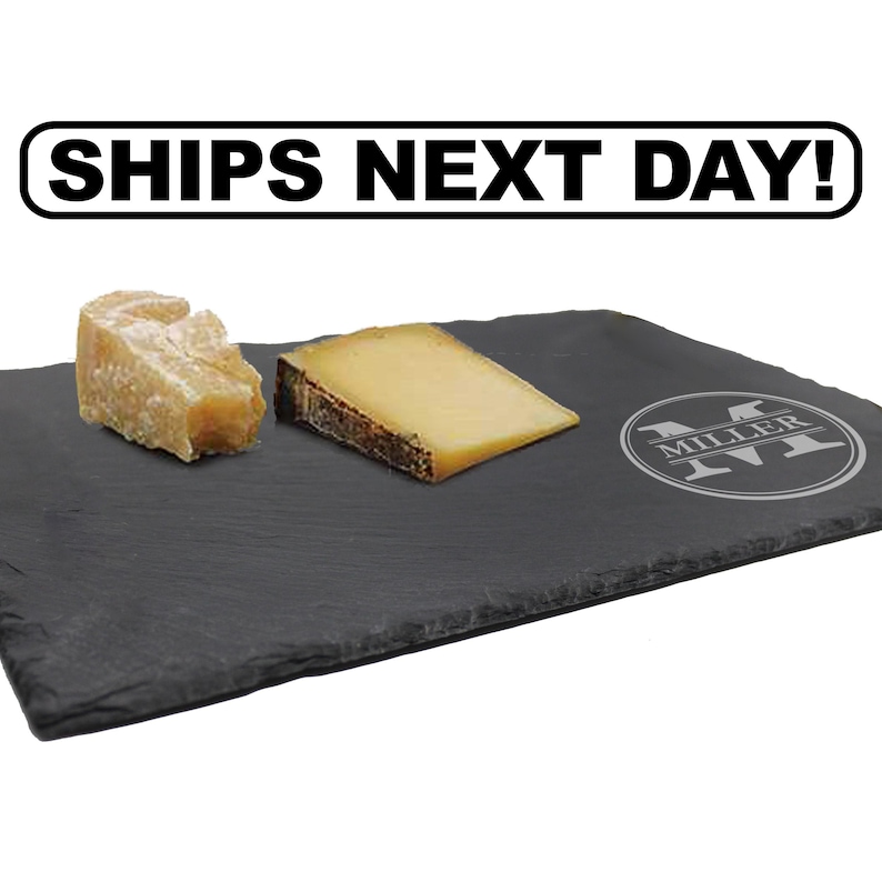 May include: A rectangular black slate serving board featuring a circular engraved monogram with the letter M and the name MILLER. Two pieces of cheese are placed on the surface. The text SHIPS NEXT DAY! is displayed in a white box above the board.