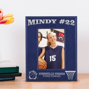 May include: A navy blue picture frame with the name "MINDY #22" in silver lettering. The frame holds a photo of two smiling basketball players. The bottom of the frame features a basketball graphic and the text "JOHNVILLE VIKINGS POWER FORWARD."