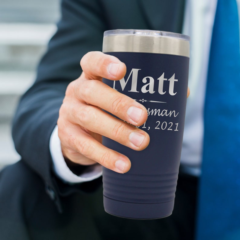 May include: A navy blue stainless steel tumbler with a silver lid. The tumbler has the name "Matt" engraved on it, along with the words "Best Man" and the date "01, 2021".
