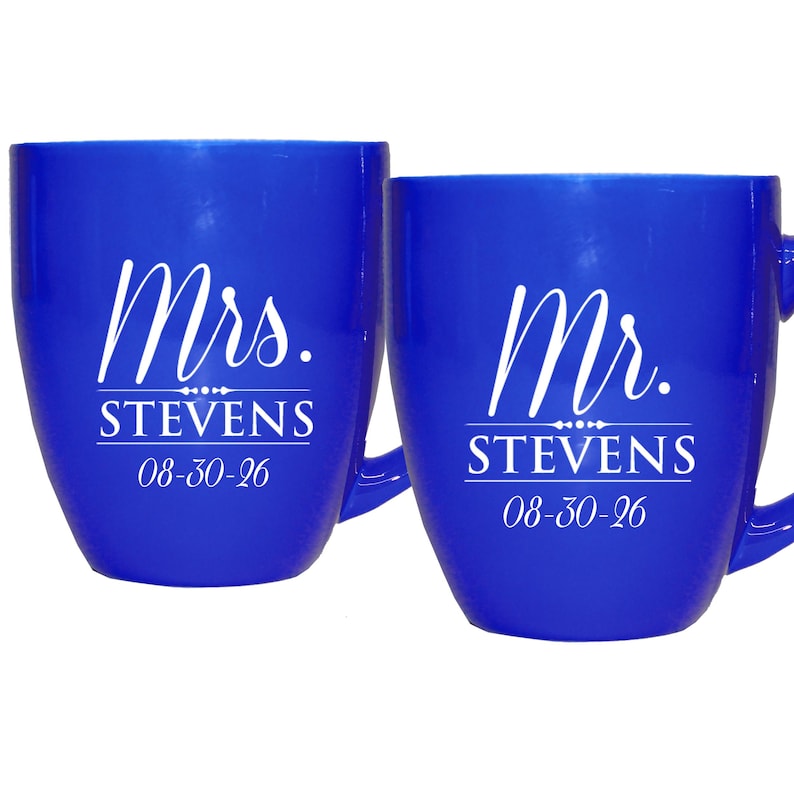 May include: Two cobalt blue mugs with white text. One mug reads "Mrs. STEVENS 08-30-26" and the other reads "Mr. STEVENS 08-30-26". The mugs have a curved shape and a handle.