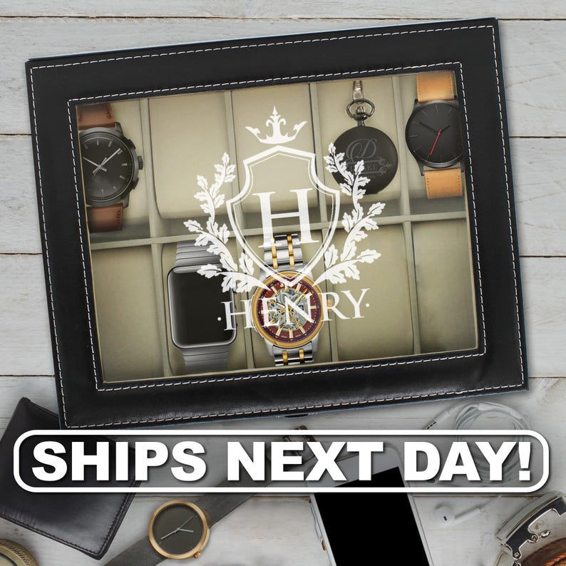 May include: A black rectangular watch display case with a glass lid featuring a white printed crest with the letter H and the name HENRY. The interior contains beige velvet cushions holding various wristwatches and a pocket watch.
