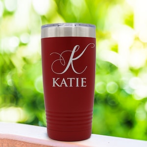 Pode incluir: Um copo t&eacute;rmico vermelho com tampa prateada. O copo apresenta o nome "KATIE" em escrita branca sob uma letra "K" branca. Projetado para manter as bebidas quentes ou frias.