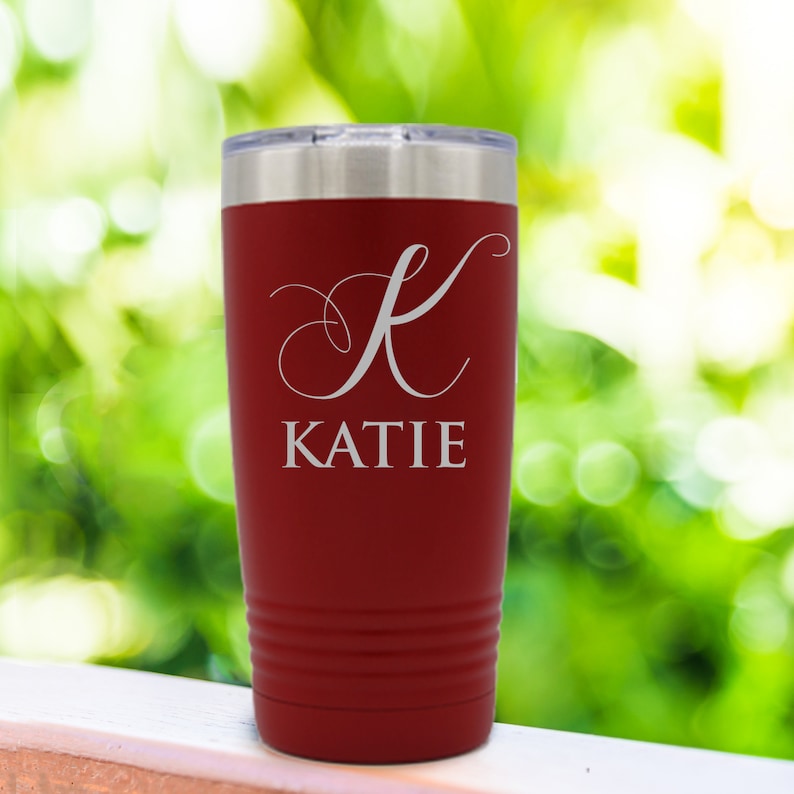 Pode incluir: Um copo t&eacute;rmico vermelho com tampa prateada. O copo apresenta o nome "KATIE" em escrita branca sob uma letra "K" branca. Projetado para manter as bebidas quentes ou frias.