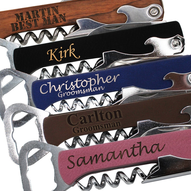 Op de afbeelding: Vijf gepersonaliseerde flessenopeners voor wijnflessen met verschillende namen en titels, waaronder "Best Man", "Groomsman" en "Samantha". De openers zijn gemaakt van hout, metaal en hebben een kurkentrekker en een flessenopener.