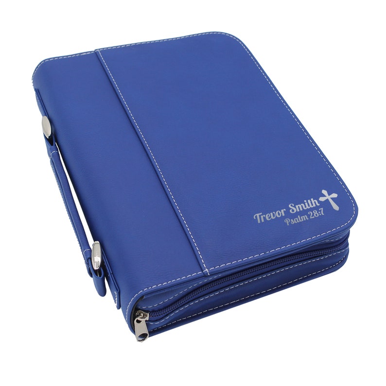 May include: A royal blue Bible cover with white stitching and a silver zipper. The cover has a handle and a cross with the text "Trevor Smith Psalm 28:7".