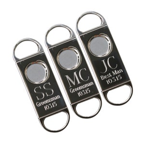 May include: Three silver cigar cutters with engraved initials and titles. The cutters are engraved with "SS  Groomsman 10315", "MC Groomsman 10315", and "JC Best Man 10315".