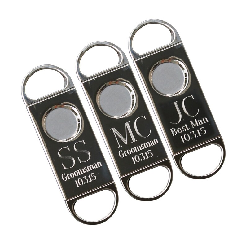 May include: Three silver cigar cutters with engraved initials and titles. The cutters are engraved with "SS  Groomsman 10315", "MC Groomsman 10315", and "JC Best Man 10315".