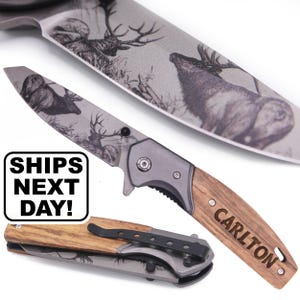 May include: A folding pocket knife with a grey metal blade featuring an engraved deer scene. The handle is made of wood with the name CARLTON engraved on the side. A second closed knife is visible below, showing a black metal pocket clip.