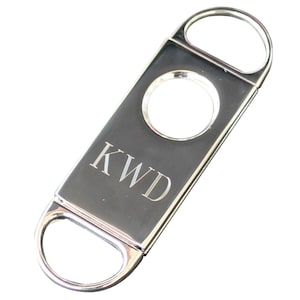 May include: Silver cigar cutter with a round blade and a personalized inscription that reads "KWD".