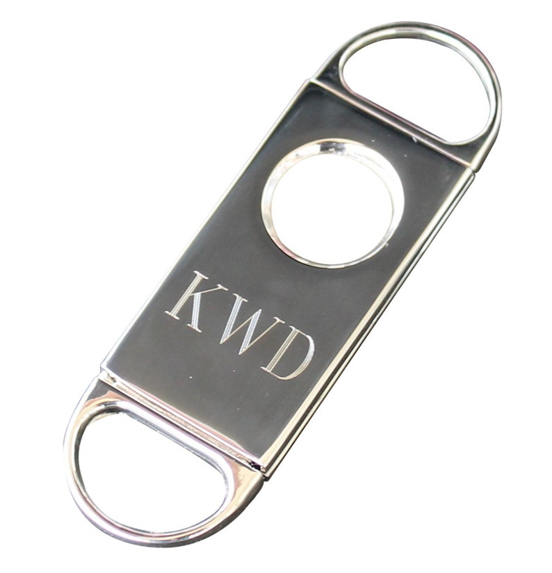 May include: Silver cigar cutter with a round blade and a personalized inscription that reads "KWD".