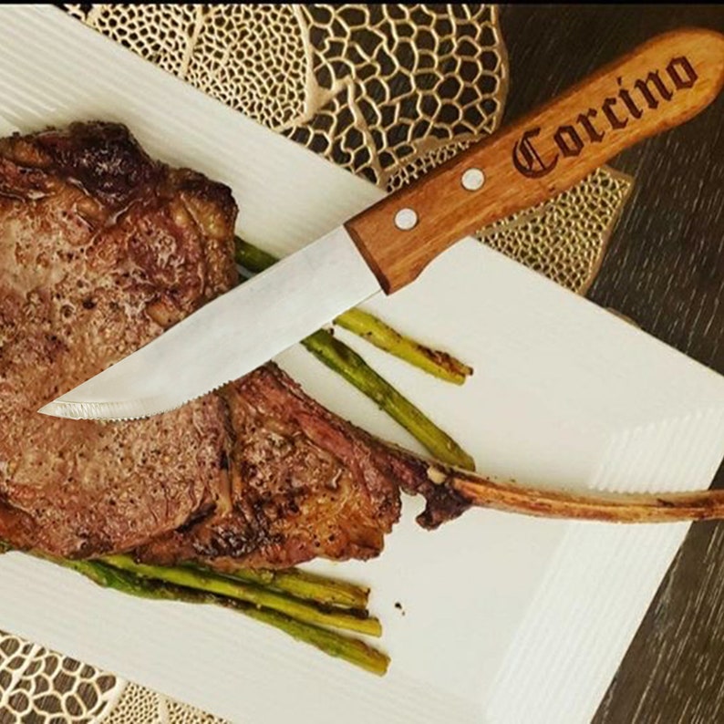 May include: A close-up of a cooked steak with asparagus on a white plate. A wooden handled steak knife with the word "Corcino" engraved on the handle is resting on the plate.