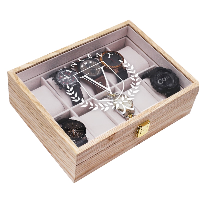May include: A wooden watch box with a clear glass top, containing several watches. The box is light brown with a gold clasp. The watches have black, brown, and silver bands. The name "VINCENT" is printed on the glass.